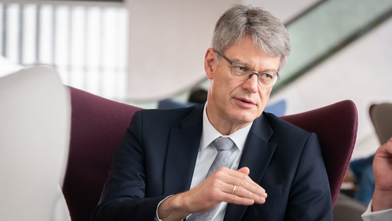 Patrick Schnieder sitzt auf einem dunkelroten Sessel, gestikuliert und spricht mit einer Person außerhalb des Bildes. Patrick Schnieder sitzt auf einem dunkelroten Sessel, gestikuliert und spricht mit einer Person außerhalb des Bildes.