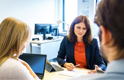 Beratungsrunde zwischen drei Personen am Schreibtisch Beratungsrunde zwischen drei Personen am Schreibtisch