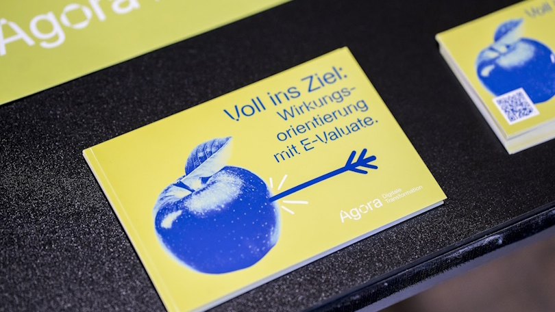 Projektfoto E-Valuate: Ein Schild mit einem Apfel, der von einem Pfeil durchbohrt wurde, und der Aufschrift "Voll ins Ziel: Wirkungsorientierung mit E-Valuate. Agora Digitale Transformation." Projektfoto E-Valuate: Ein Schild mit einem Apfel, der von einem Pfeil durchbohrt wurde, und der Aufschrift "Voll ins Ziel: Wirkungsorientierung mit E-Valuate. Agora Digitale Transformation."