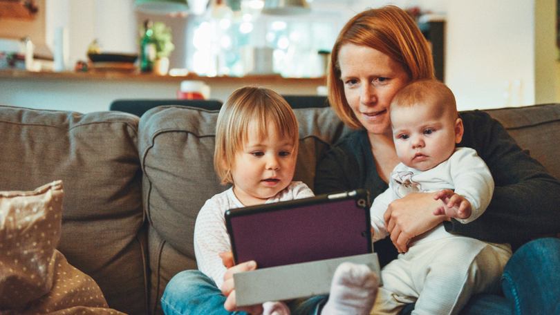 Eine Mutter guckt auf der Couch zu Hause mit ihren Kinder auf ein Tablet Eine Mutter guckt auf der Couch zu Hause mit ihren Kinder auf ein Tablet