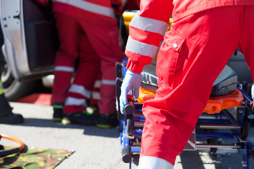 Ersthelfer in roten Overalls schieben eine Trage zu verunfalltem Auto Ersthelfer in roten Overalls schieben eine Trage zu verunfalltem Auto