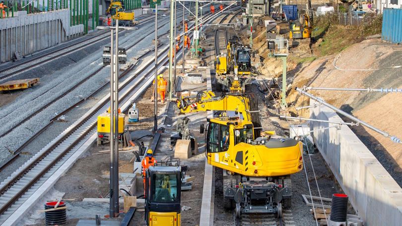 Baustelle an Schienen mit vielen gelben Baumaschinen und einem Bagger Baustelle an Schienen mit vielen gelben Baumaschinen und einem Bagger