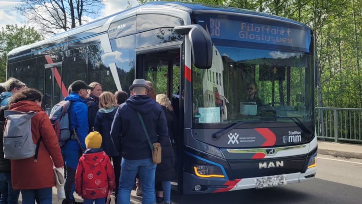 Mehrere menschen stehen vor einem Bus mit der Aufschrift Pilotfahrt Glasiusweg Mehrere menschen stehen vor einem Bus mit der Aufschrift Pilotfahrt Glasiusweg