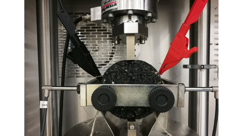 Sensorierter Asphaltprobenkörper in einer Prüfmaschine Sensorierter Asphaltprobenkörper in einer Prüfmaschine