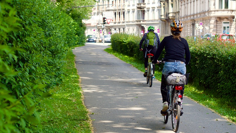 Zwei Radfahrer auf einem städtischen Fahrradweg umgeben von Bäumen und Sträuchern Zwei Radfahrer auf einem städtischen Fahrradweg umgeben von Bäumen und Sträuchern