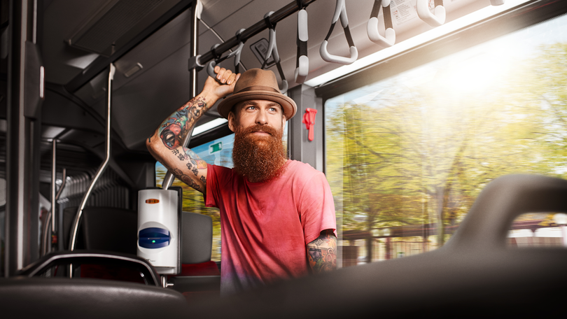 Ein junger Mann mit Hut fährt in einem Bus und hält sich an einem Haltegriff fest Ein junger Mann mit Hut fährt in einem Bus und hält sich an einem Haltegriff fest