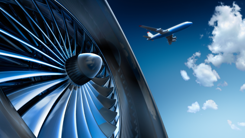 Nahaufnahme einer Turbine, im Hintergrund fliegt ein Flugzeug Nahaufnahme einer Turbine, im Hintergrund fliegt ein Flugzeug