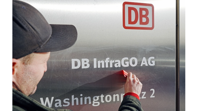 Mann klebt den Schriftzug DB InfraGo AG Mann klebt den Schriftzug DB InfraGo AG