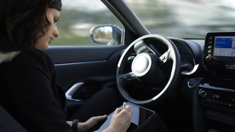 Eine Frau sitzt am Steuer und bedient während der Fahrt ein Tablet Eine Frau sitzt am Steuer und bedient während der Fahrt ein Tablet