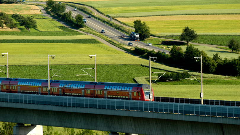Landschaftsfoto mit einer fahrenden Eisenbahn und einer Straße im Hintergrund Landschaftsfoto mit einer fahrenden Eisenbahn und einer Straße im Hintergrund