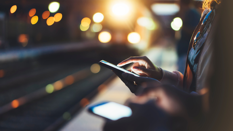 Frau die auf einem Bahnsteig bei Abendlicht auf ihr Handy schaut Frau die auf einem Bahnsteig bei Abendlicht auf ihr Handy schaut