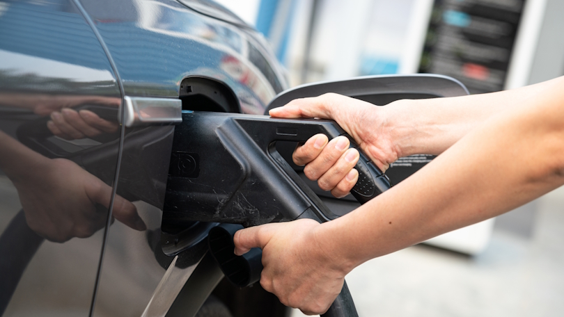 Eine Person schließt ein Elektroauto zum Laden an eine Schnellladesäule an. Im Hintergrund ist die Ladesäule zu sehen. Der Fokus liegt auf der Nahaufnahme der Hände mit dem Stecker. Eine Person schließt ein Elektroauto zum Laden an eine Schnellladesäule an. Im Hintergrund ist die Ladesäule zu sehen. Der Fokus liegt auf der Nahaufnahme der Hände mit dem Stecker.