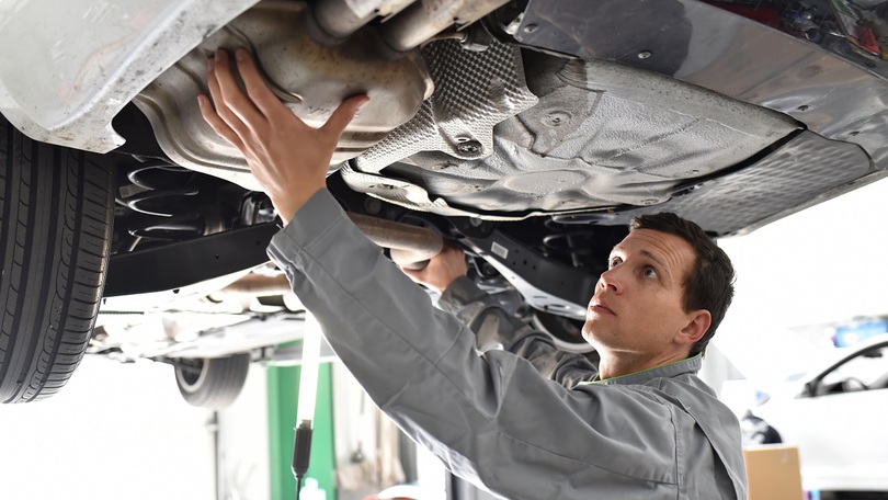 Ein Mechaniker arbeitet am Unterboden eines Kraftfahrzeugs Ein Mechaniker arbeitet am Unterboden eines Kraftfahrzeugs