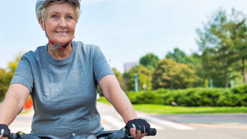 Eine ältere Dame mit Fahrradhelm fährt lächelnd auf einem Fahrrad Eine ältere Dame mit Fahrradhelm fährt lächelnd auf einem Fahrrad
